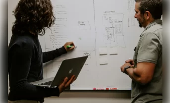 Two people looking at the blackboard, doing research and writing things down